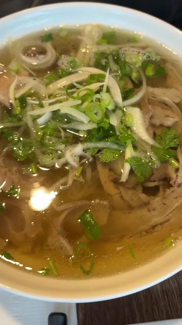 A bowl of pho with sliced beef, herbs and noodles in a rich broth